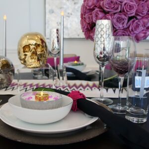 A table setting with a gold skill, glasses, cutlery, and a violet flower arrangement